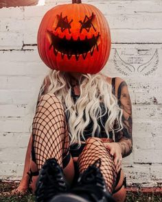 a woman sitting on the ground wearing fishnet stockings and holding a pumpkin over her head