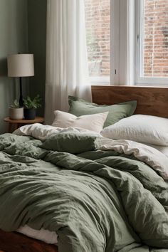 an unmade bed with green sheets and pillows in front of a large windowsill