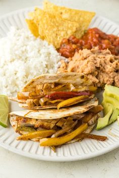 a white plate topped with lots of food next to rice and avocado wedges