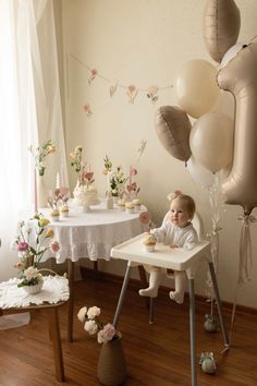 a baby is sitting in a high chair with balloons and flowers on the table next to it