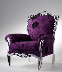 an ornate purple chair with silver trimmings on the arm and back, in front of a gray background