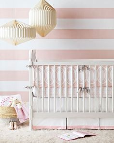 a baby crib with pink and white striped wallpaper in the background, next to a teddy bear