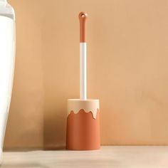 an orange and white toothbrush holder next to a vase on a beige wall background