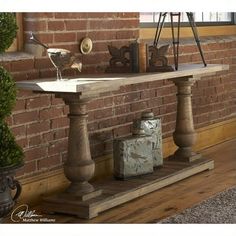 an old fashioned wooden table in front of a brick wall with various items on it