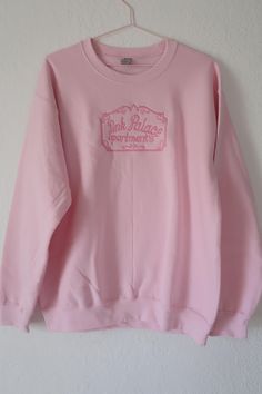 a pink sweatshirt hanging on a wall with the words pink palace written in white ink