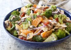 a blue bowl filled with broccoli, oranges and other vegetables on top of a table