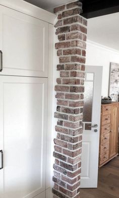 a tall brick pillar in the middle of a room with white cupboards and drawers