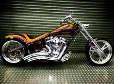 a chrome motorcycle parked in front of a garage door with an orange and purple paint job