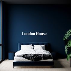 a bedroom with blue walls and white bedding in the foreground is a large window that reads london house