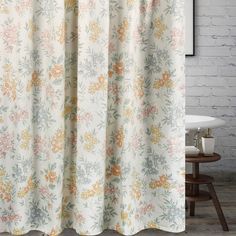 a white shower curtain with colorful flowers on it in front of a brick wall and wooden floor