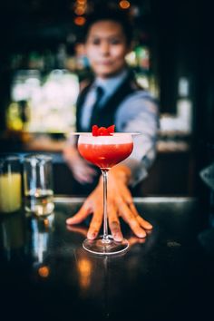 a person standing behind a bar with a cocktail in front of them and the bartender's hand on the counter