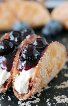 two pastries with blueberries and cream on them are sitting on a black surface