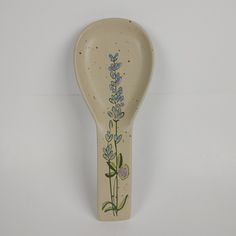 a ceramic spoon with a flower painted on it's side, hanging from the wall