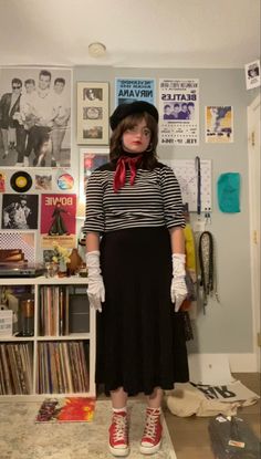 a woman standing in front of a wall with pictures on it and wearing red shoes