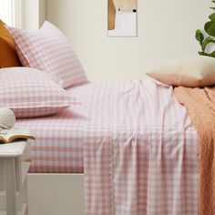 a bed with pink and white checkered bedspread next to a potted plant