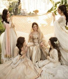 four women dressed in white sitting on the ground with one woman wearing a long dress