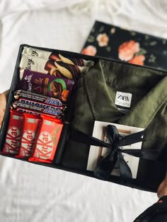 a person holding an open suitcase filled with snacks and candy bars on top of a bed