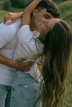 a man and woman are hugging in the grass with their arms around each other as they hug