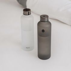 two water bottles sitting next to each other on a white tablecloth covered bed with pillows