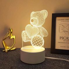 a light up teddy bear sitting on top of a table next to a framed photo