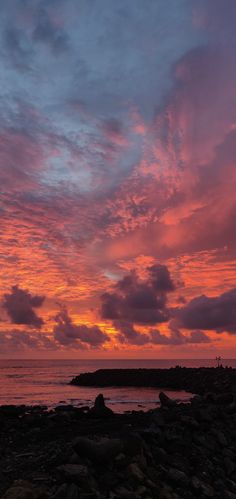 the sky is pink and blue as it sets over the ocean with rocks on the shore