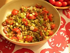 a bowl filled with vegetables sitting on top of a red and white table cloth next to tomatoes