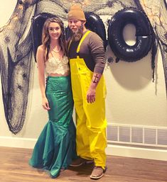 a man and woman dressed up in costumes standing next to each other with balloons on the wall behind them