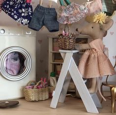 a teddy bear sitting on top of a wooden stool next to a dryer and clothes