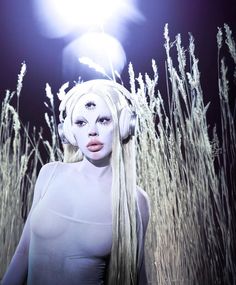 a woman with white hair and headphones standing in tall grass under a street light