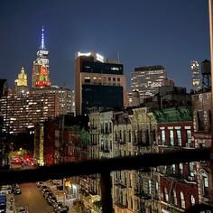 the city skyline is lit up at night, with buildings in the foreground and cars parked on the street below