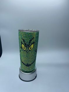 a green cup with yellow eyes is sitting on a silver stand next to a black bag