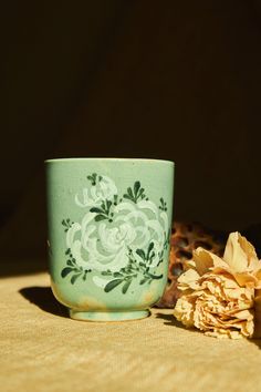 a green cup sitting on top of a table next to a flower