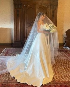 a woman in a wedding dress and veil is standing on the floor with her bouquet