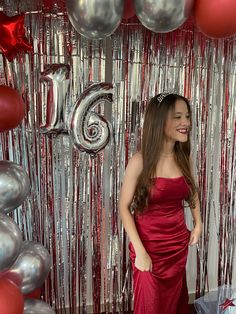 a woman in a red dress standing next to balloons and streamers with the number six on it