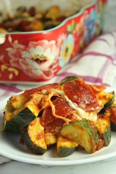 a white plate topped with zucchini and pepperoni covered in sauce next to a casserole dish