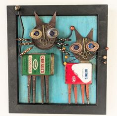 two cats made out of old toothbrushes and tin cans are on display in a black frame