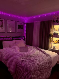 a bed in a room with purple lights on the wall and pictures hanging above it