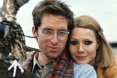 a man and woman with an owl perched on their arm, both looking at the camera