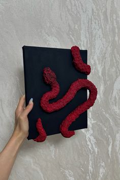 a hand holding up a piece of art made out of red yarn and paper with the letter s on it