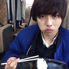 a young man eating sushi with chopsticks in his hand and looking at the camera