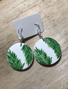 a pair of earrings with green leaves painted on the front and back of each earring