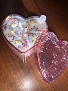 a heart shaped box filled with flowers on top of a wooden table next to a candle