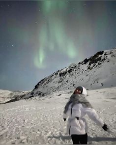 a person standing in the snow with an aurora behind them