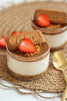 two desserts with strawberries and cookies in them sitting on a table next to a spoon