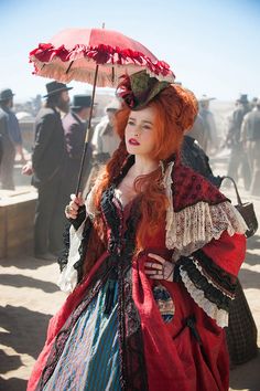 a woman with red hair is dressed in period clothing and holds an umbrella over her head