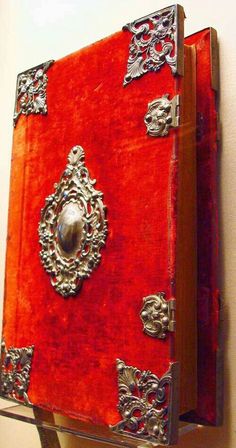 an old red book with ornate silver decorations on the front and sides, hanging from a wall