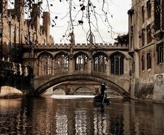 a person on a small boat in the water under a bridge with old buildings behind it