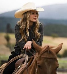 a woman riding on the back of a brown horse wearing a cowboy hat and black shirt