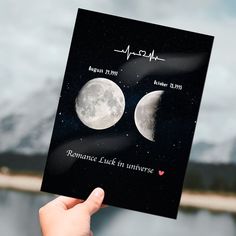 someone holding up a card with the moon and heartbeat on it in front of a lake