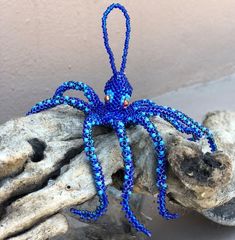 a blue beaded octopus sitting on top of a piece of driftwood next to some rocks